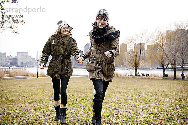 Lächelnde Freundinnen halten sich an den Händen und gehen über ein Grasfeld