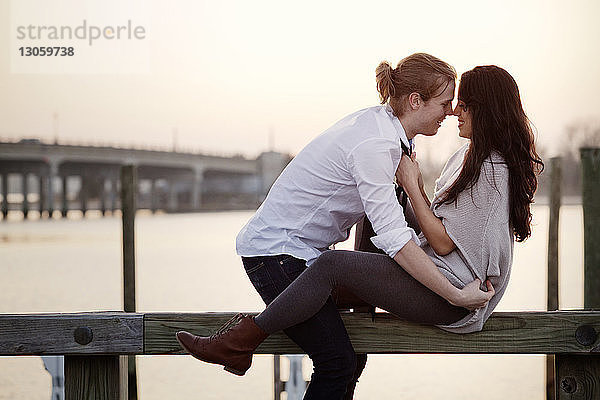 Glückliches romantisches Paar sitzt auf einem Geländer gegen den Himmel