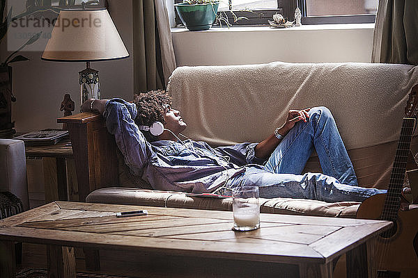 Mann hört Musik  während er sich zu Hause auf dem Sofa entspannt