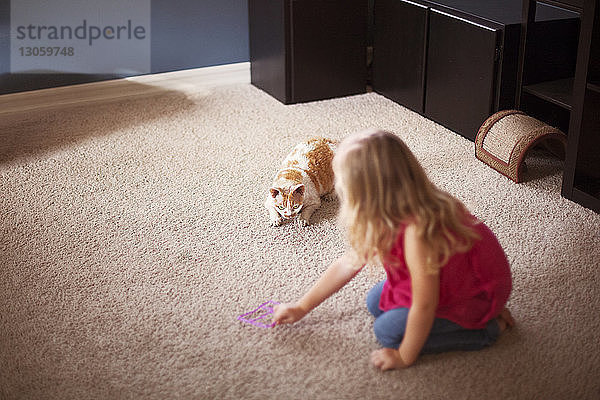 Mädchen spielt zu Hause mit Katze auf dem Teppich