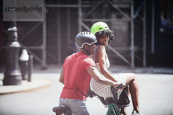 Mann radelt  während die Frau in der Stadt auf einem Fahrradkorb sitzt