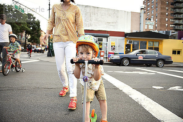 Porträt eines Jungen  der mit seiner Familie auf Straßen in der Stadt Roller fährt