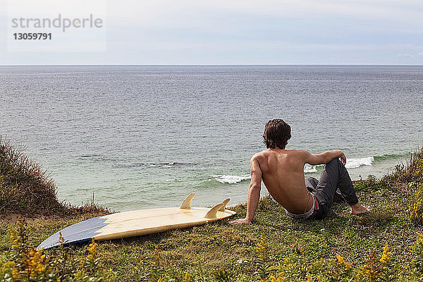 Mann mit Surfbrett entspannt sich auf dem Feld am Strand
