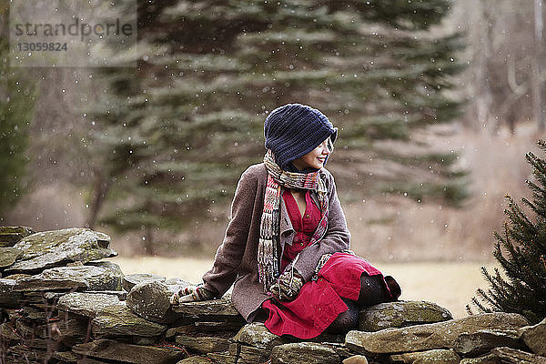 Glückliche Frau schaut weg  während sie sich auf einer Steinmauer entspannt