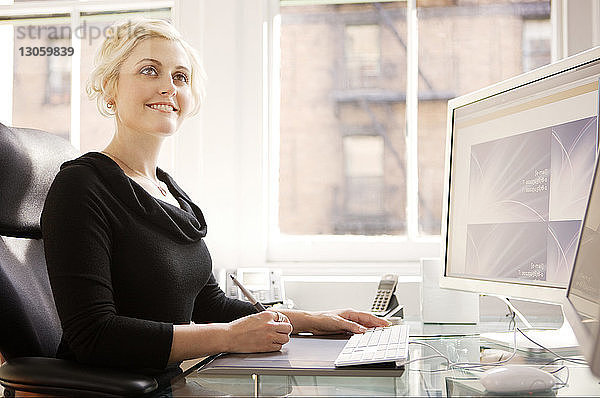 Lächelnde Geschäftsfrau benutzt Computer auf dem Tisch im Büro
