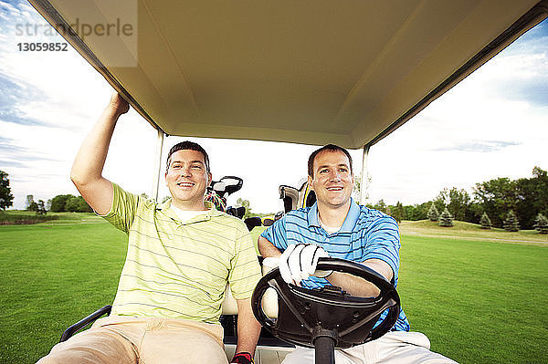 Glücklicher Golfer fährt Golfwagen  während er mit einem Freund zusammensitzt