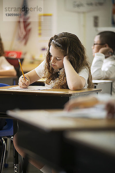 Schulmädchen schreibt Test  während sie im Klassenzimmer am Schreibtisch sitzt