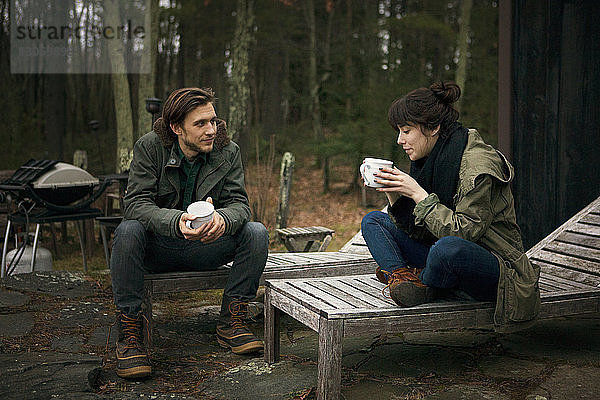Paar mit Kaffeetassen  das auf einem Liegestuhl auf dem Campingplatz sitzt