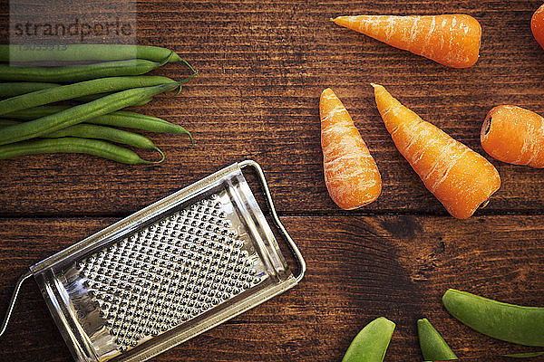 Draufsicht auf grüne Bohnen und Karotten mit Reibe auf Holztisch