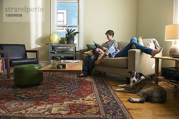Lesbisches Paar liest Zeitschrift  während es sich zu Hause auf dem Sofa entspannt