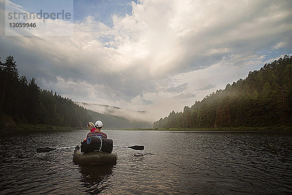 Freunde beim River Rafting gegen bewölkten Himmel