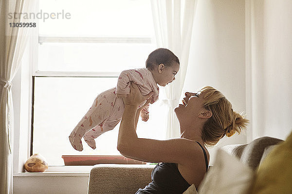 Glückliche Mutter hebt Babymädchen an  während sie zu Hause auf dem Sofa sitzt