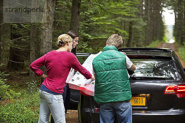 Freunde lesen Karte  während sie im Wald am Auto stehen