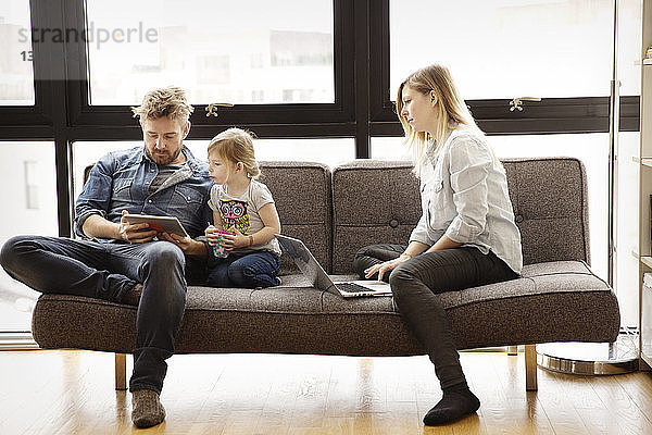 Familie nutzt Technologien  während sie zu Hause auf dem Sofa sitzt