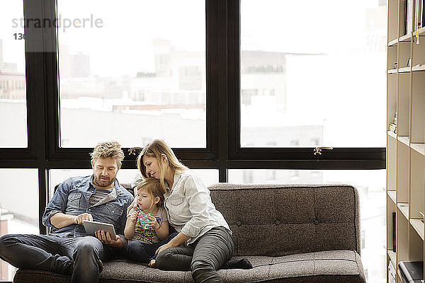Familie benutzt Tablet-Computer  während sie zu Hause auf dem Sofa sitzt