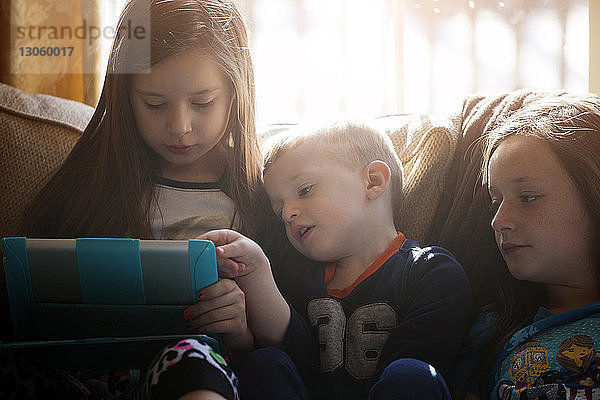 Geschwister schauen auf die Tablette  während sie zu Hause auf dem Sofa sitzen