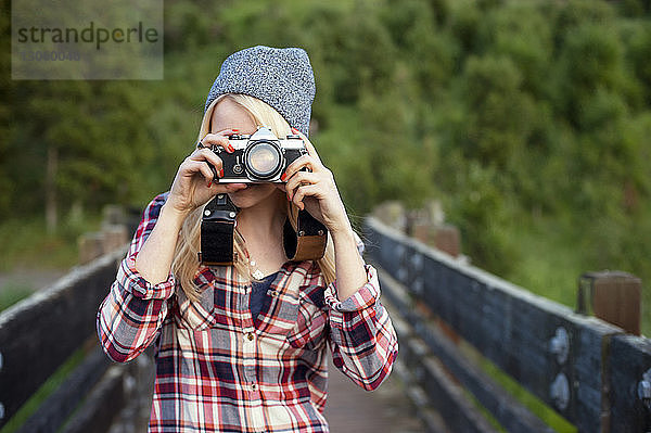 Frau fotografiert mit Kamera  während sie auf der Brücke steht