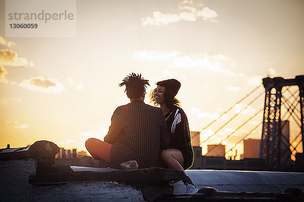 Fröhliches Paar sitzt bei Sonnenuntergang auf Stützmauer