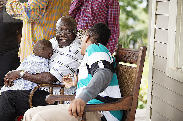 Glücklicher älterer Mann sitzt mit Enkeln auf der Veranda