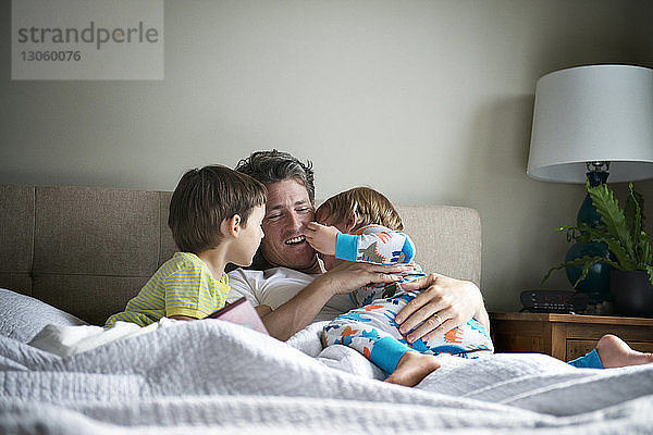 Glücklicher Vater entspannt sich mit Söhnen zu Hause im Bett