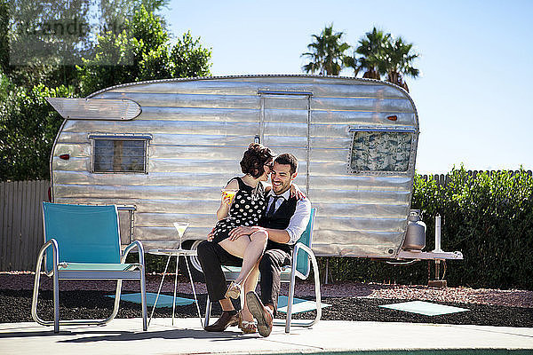 Fröhliches Paar sitzt auf Stuhl gegen Wohnmobil