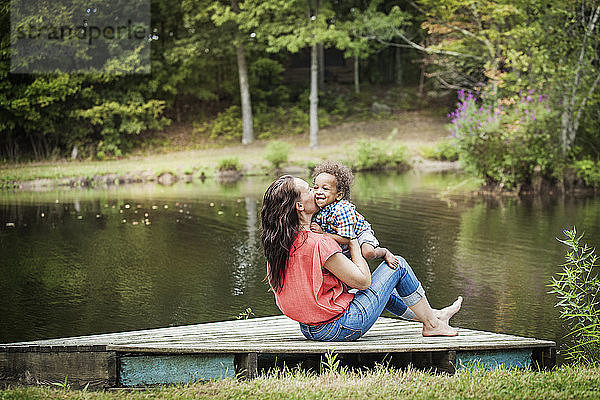 Mutter küsst Sohn  während sie auf dem Steg am See sitzt