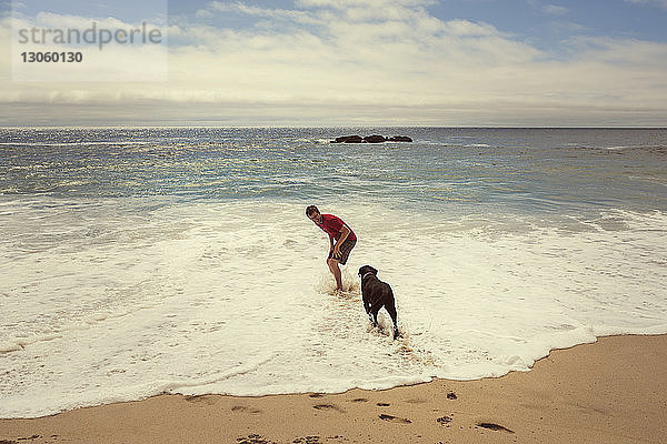 Mann spielt mit Hund auf Wellen am Ufer