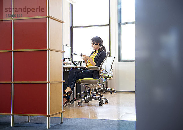 Textnachrichten einer Frau  die auf einem Stuhl am Schreibtisch im Büro sitzt
