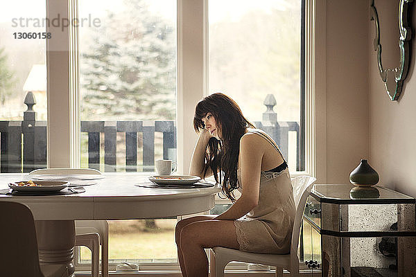 Seitenansicht einer Frau  die zu Hause auf einem Stuhl am Tisch sitzt