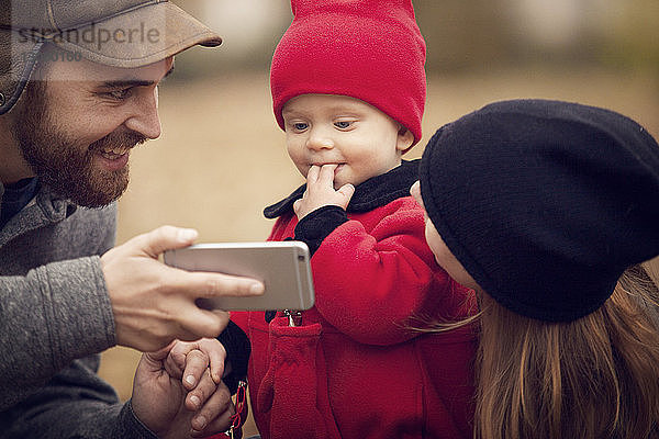 Vater zeigt dem Baby im Park ein Smartphone