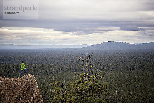 Frau schaut auf Wald  während sie auf einem Felsen vor bewölktem Himmel steht