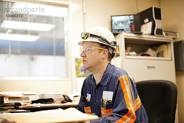 Seitenansicht eines reifen männlichen Arbeiters  der in einer Recycling-Anlage am Tisch sitzt