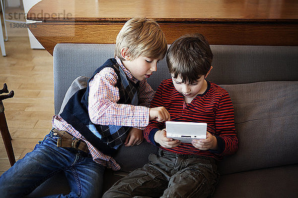 Hochwinkelansicht von Geschwistern  die zu Hause auf dem Sofa sitzen und Videospiele spielen