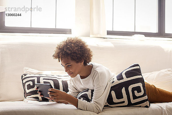 Mädchen benutzt Tablet-Computer  während sie zu Hause auf dem Sofa liegt