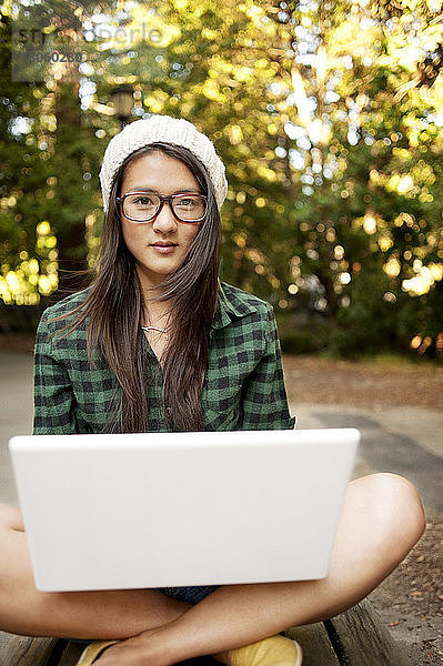 Porträt einer Frau  die mit Laptop-Computer auf dem Feld sitzt