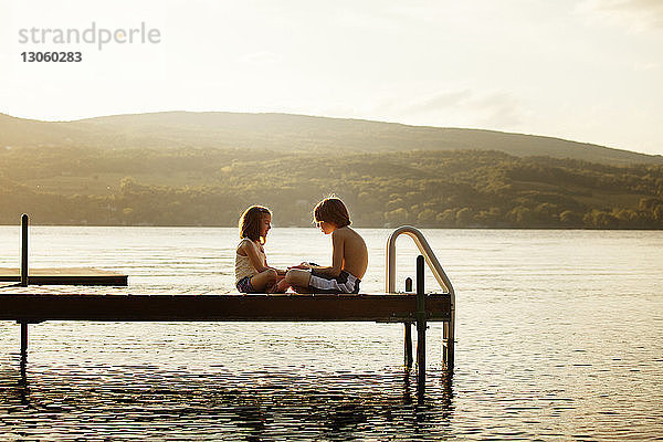 Seitenansicht der Geschwister beim Spielen auf dem Steg über dem See an einem sonnigen Tag