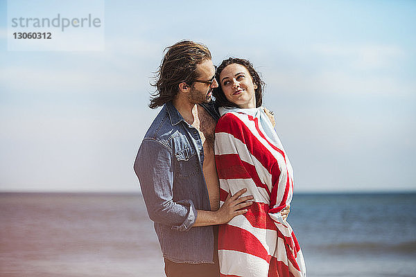 Seitenansicht eines romantischen Mannes  der mit einer in eine Decke gehüllten Frau am Strand steht