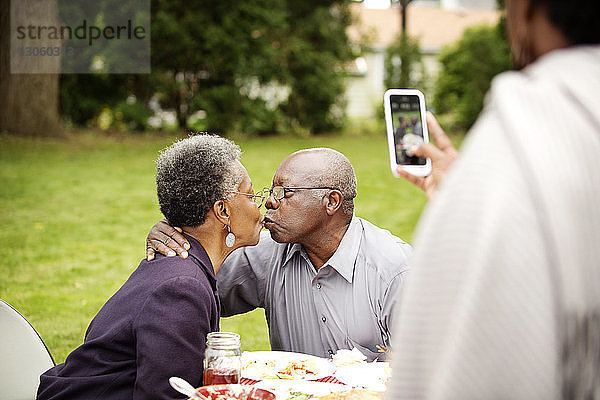 Ausschnitt einer Frau  die ein älteres Paar beim Küssen im Garten fotografiert