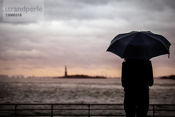 Rückansicht einer Frau mit Regenschirm vor bewölktem Himmel stehend