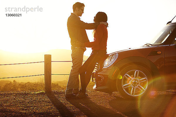 Paar umarmt sich  während es im Auto auf dem Feld gegen den Himmel steht