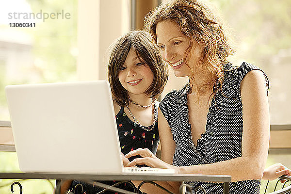 Mutter und Tochter benutzen Laptop-Computer  während sie zu Hause sitzen