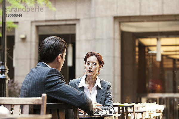 Geschäftsmann und Geschäftsfrau diskutieren  während sie im Straßencafé sitzen