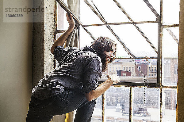 Mann schaut durch Fenster  während er zu Hause steht