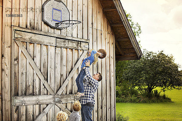 Glücklicher Vater trägt Tochter  während er mit Kindern Basketball spielt