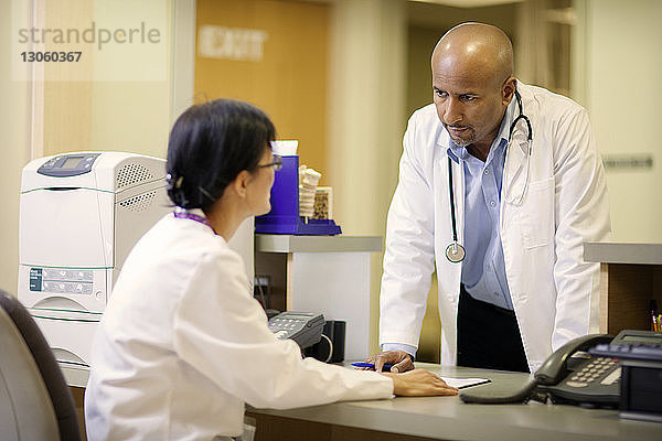 Männlicher Arzt bespricht sich mit weiblicher Ärztin am Schreibtisch im Krankenhaus