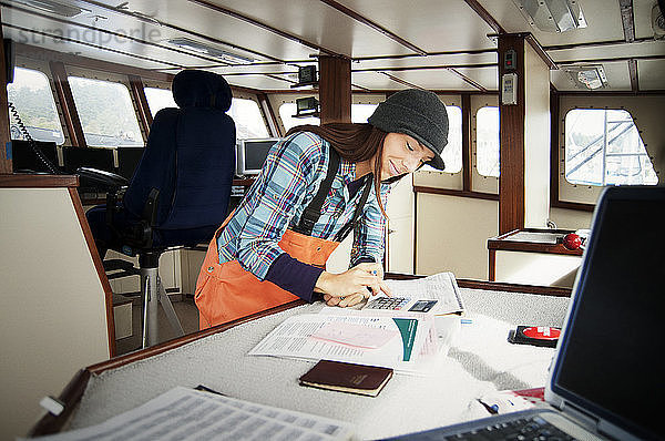 Frau benutzt Taschenrechner und schreibt auf Dokumente im Fischerboot