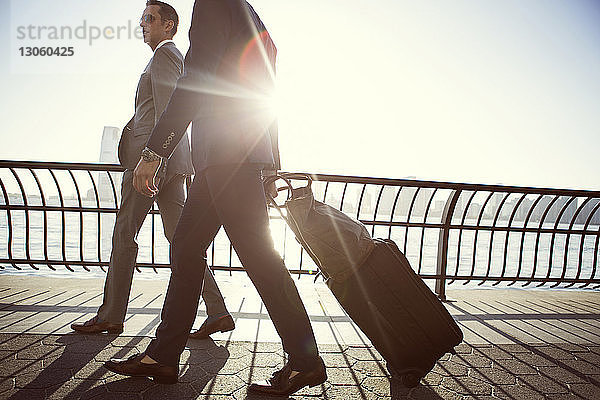 Geschäftsleute mit Gepäck gehen bei Sonnenschein auf der Promenade