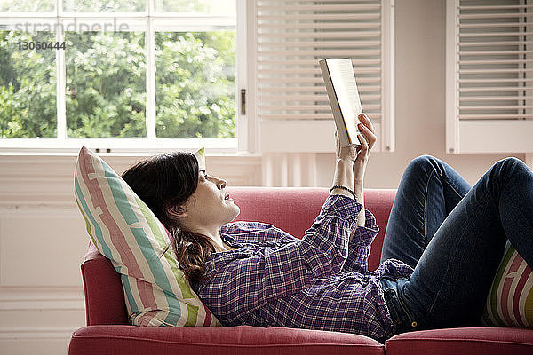 Frau liest Buch im Liegen auf dem Sofa