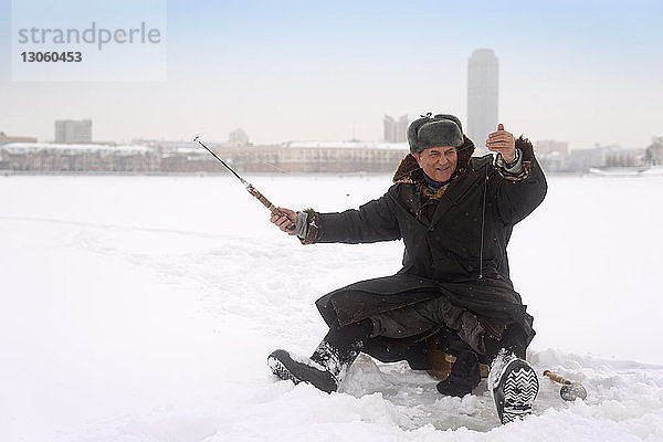 Glücklicher Mann beim Eisfischen im zugefrorenen See
