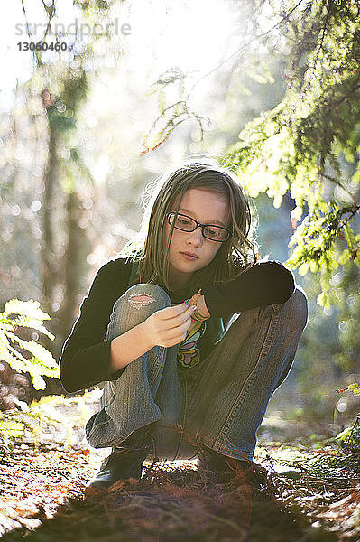 Mädchen betrachtet trockenes Blatt im Wald an einem sonnigen Tag